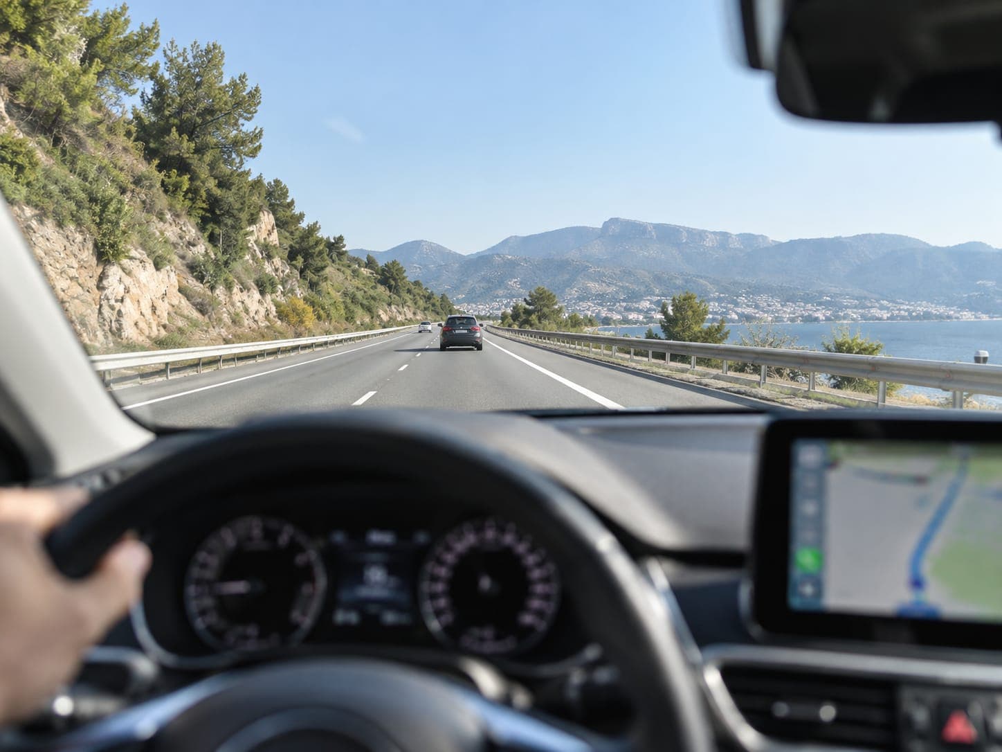 Vista desde el asiento del conductor en una carretera de costa: la carretera se ve nítida y el salpicadero y la pantalla del coche, borrosos
